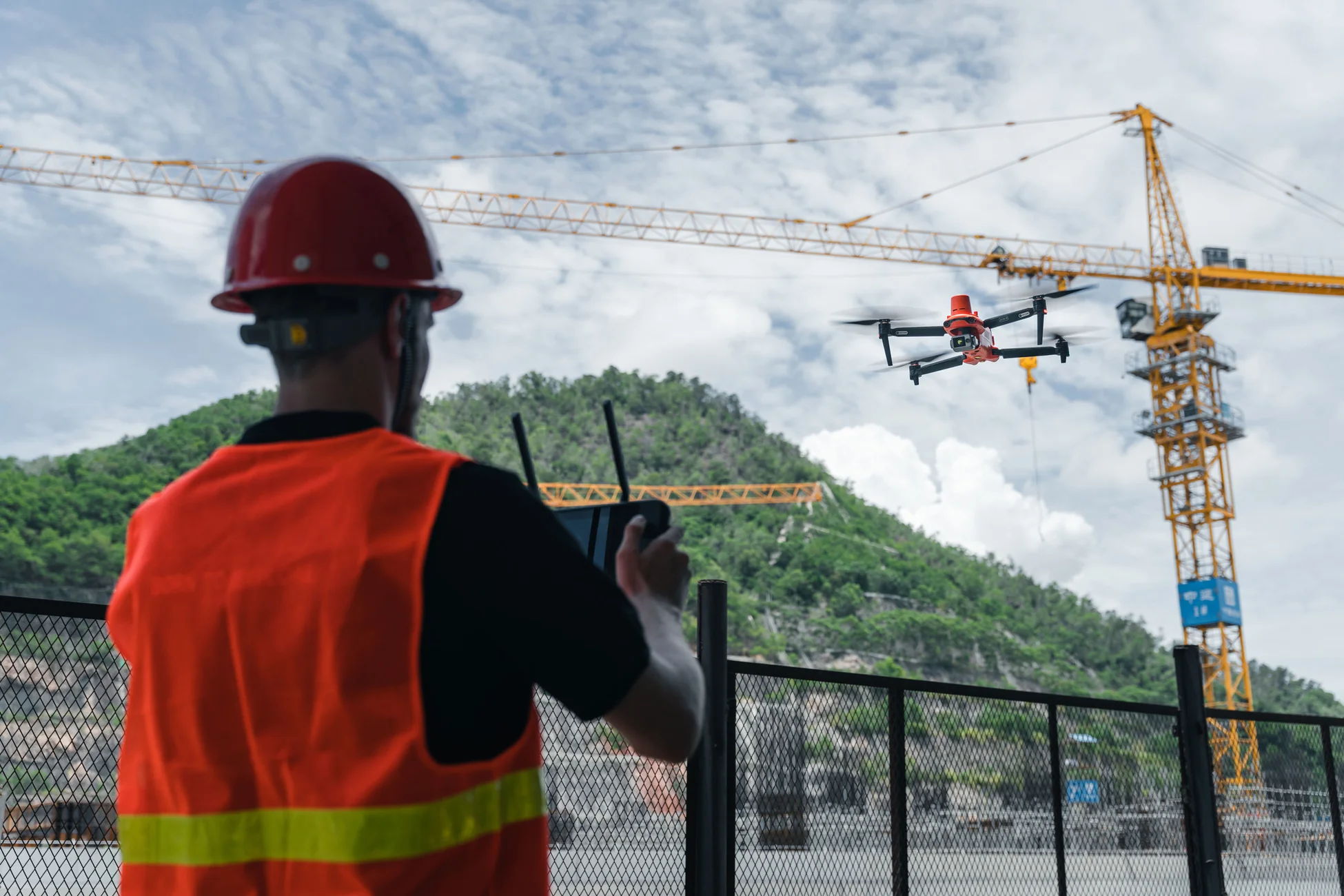 Person in safety gear operating a drone near a construction site.
