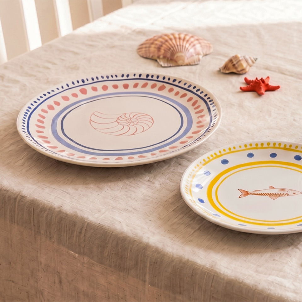 Two decorative plates on a light tablecloth with seashells and a starfish.