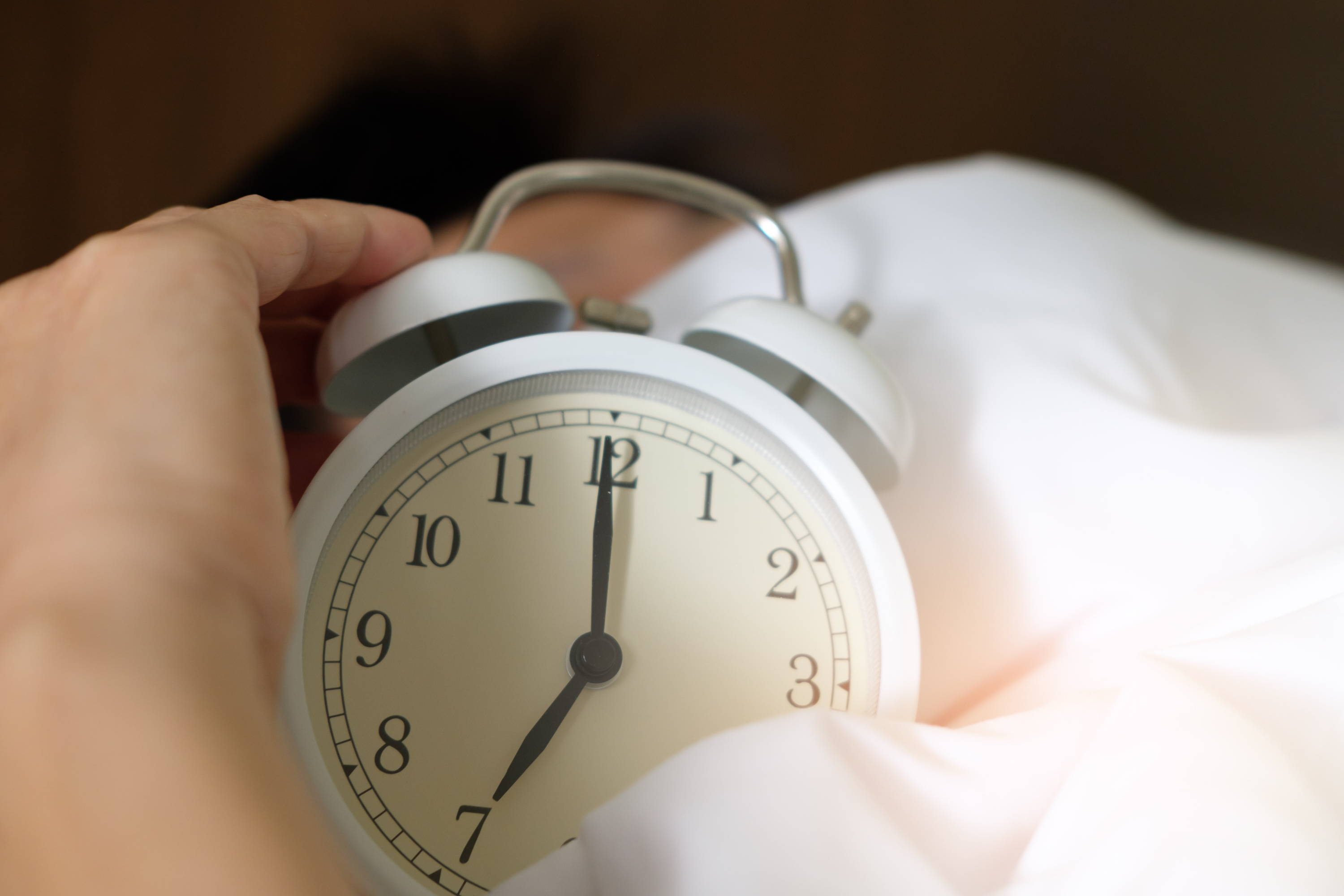 A white analog alarm clock partially wrapped in a white sheet