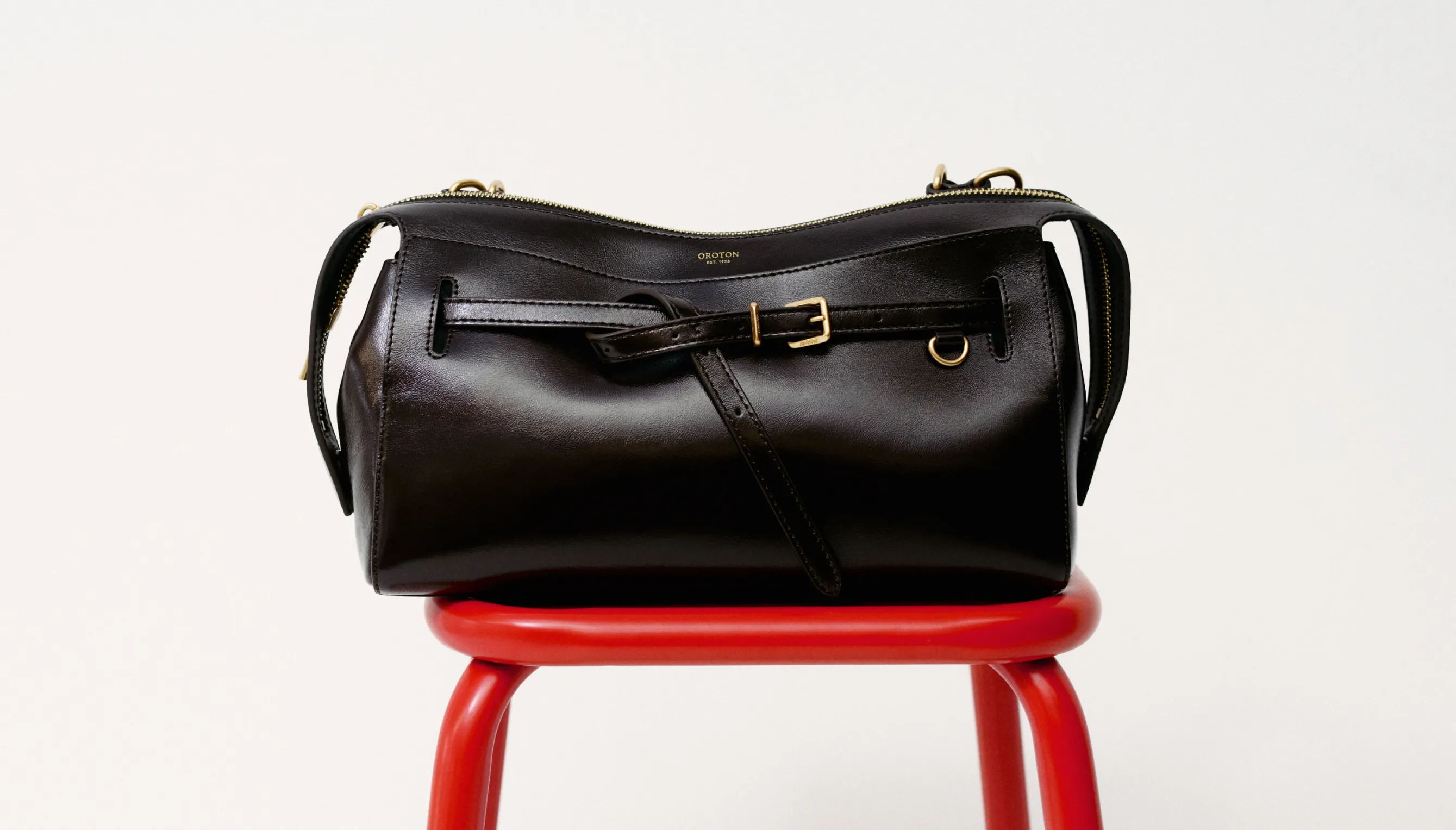 Black leather bag resting on a red stool against a white background.