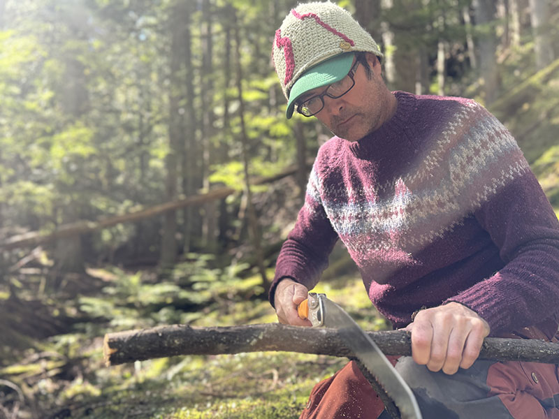 Person cutting a stick in a forested area.