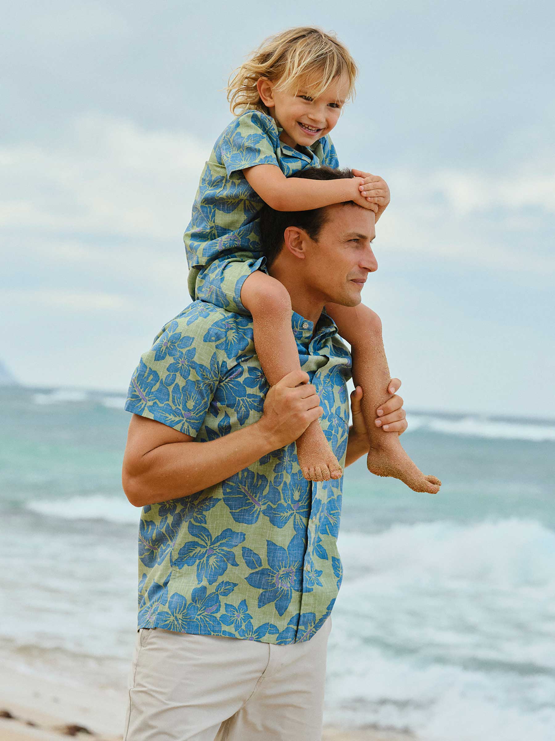 Man carrying a child on his shoulders at the beach.