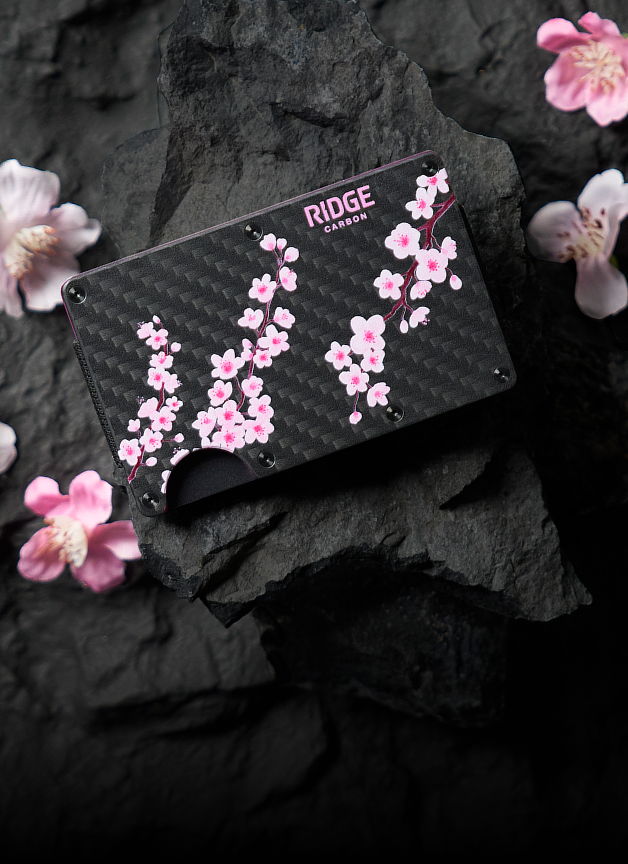 Black wallet with pink cherry blossom design on a textured surface.