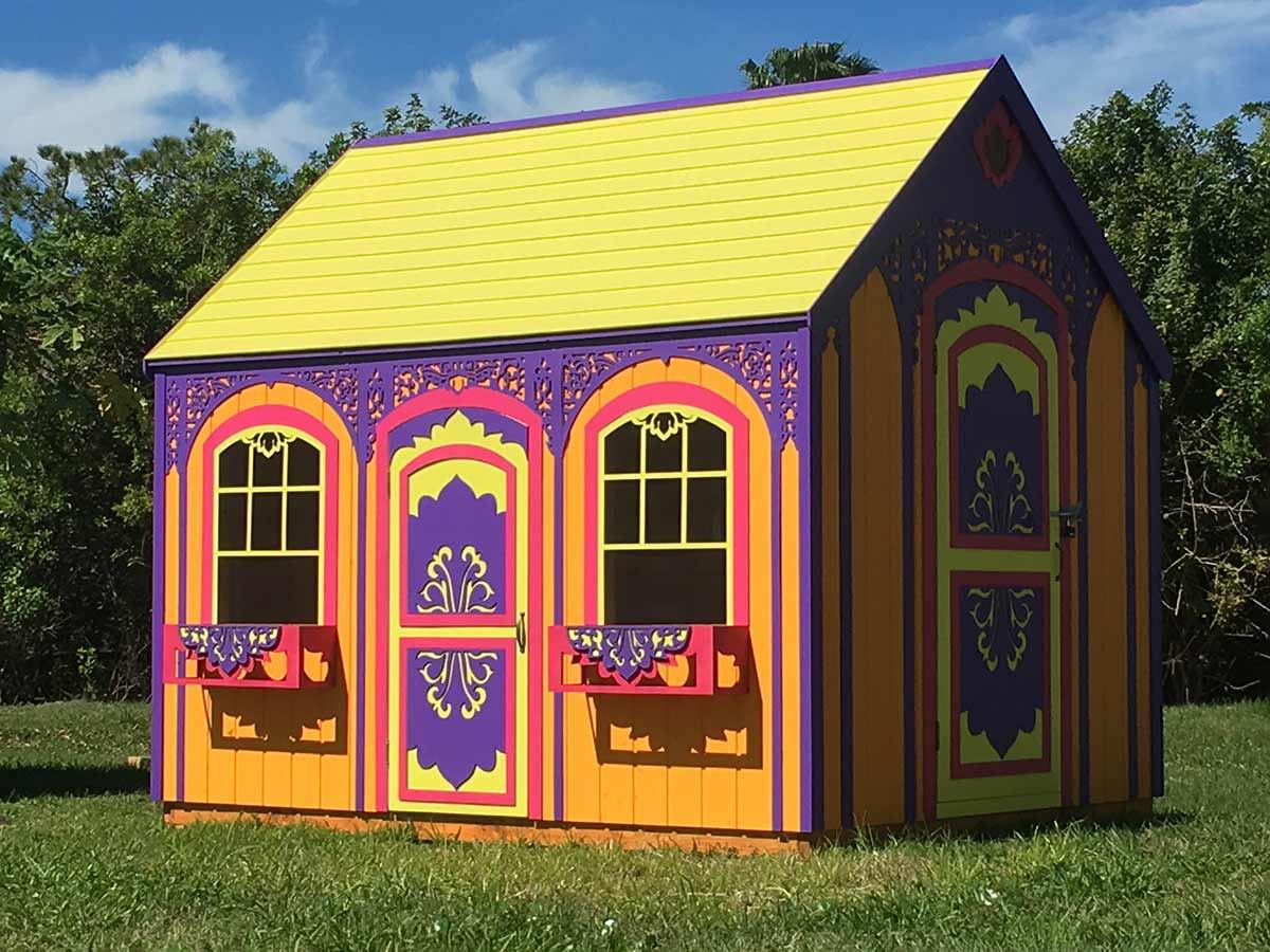 Custom playhouse in bright colors and yellow roof on green grass and blue sky at the back by WholeWoodPlayhouses