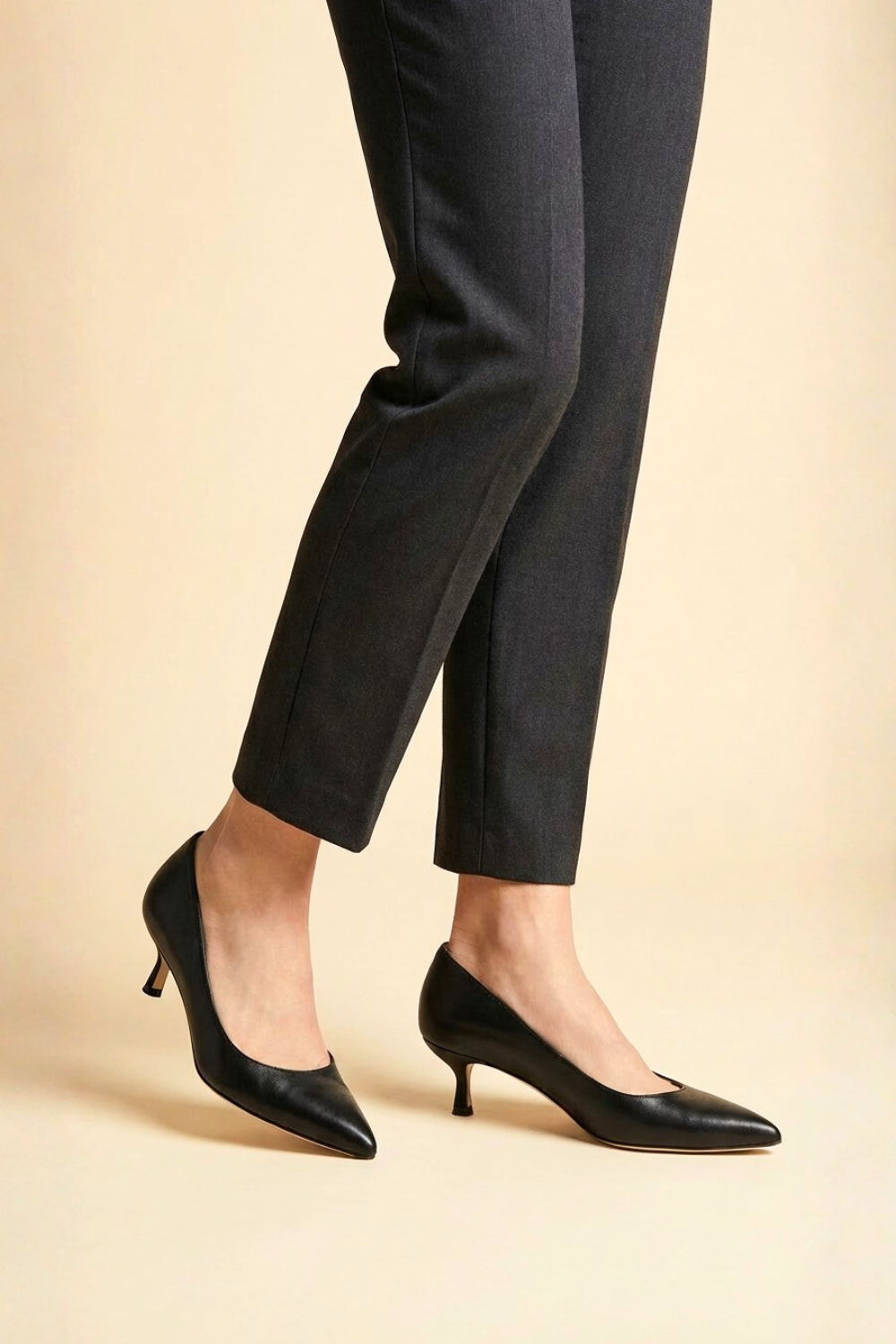 Woman wearing black high-heeled shoes and dark pants against a neutral background.