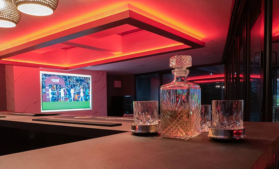 A stylish bar with a decanter, glasses, and a TV showing a game.