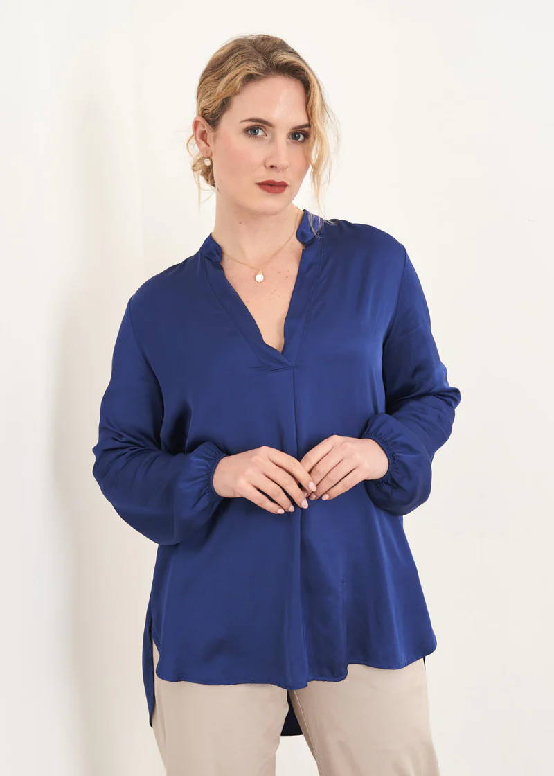 A model wearing a dark blue satin blouse with v neck and off white trousers