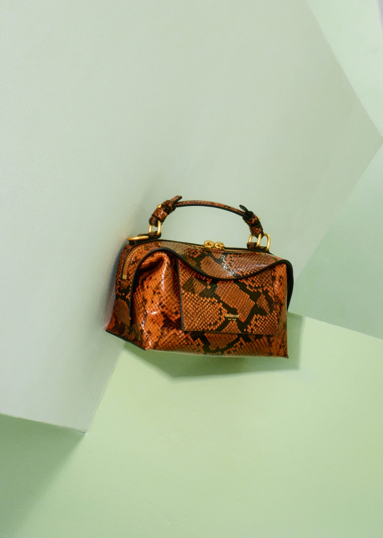 A stylish orange snakeskin handbag on a light green background.