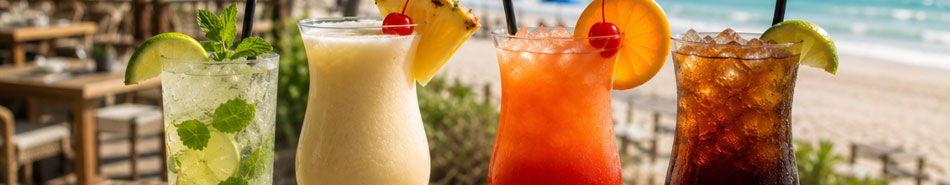 Four colorful cocktails on a beachside table with ocean view.