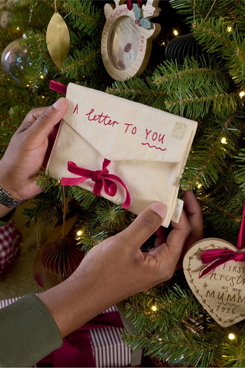 Hands holding a letter tied with a ribbon on a Christmas tree.