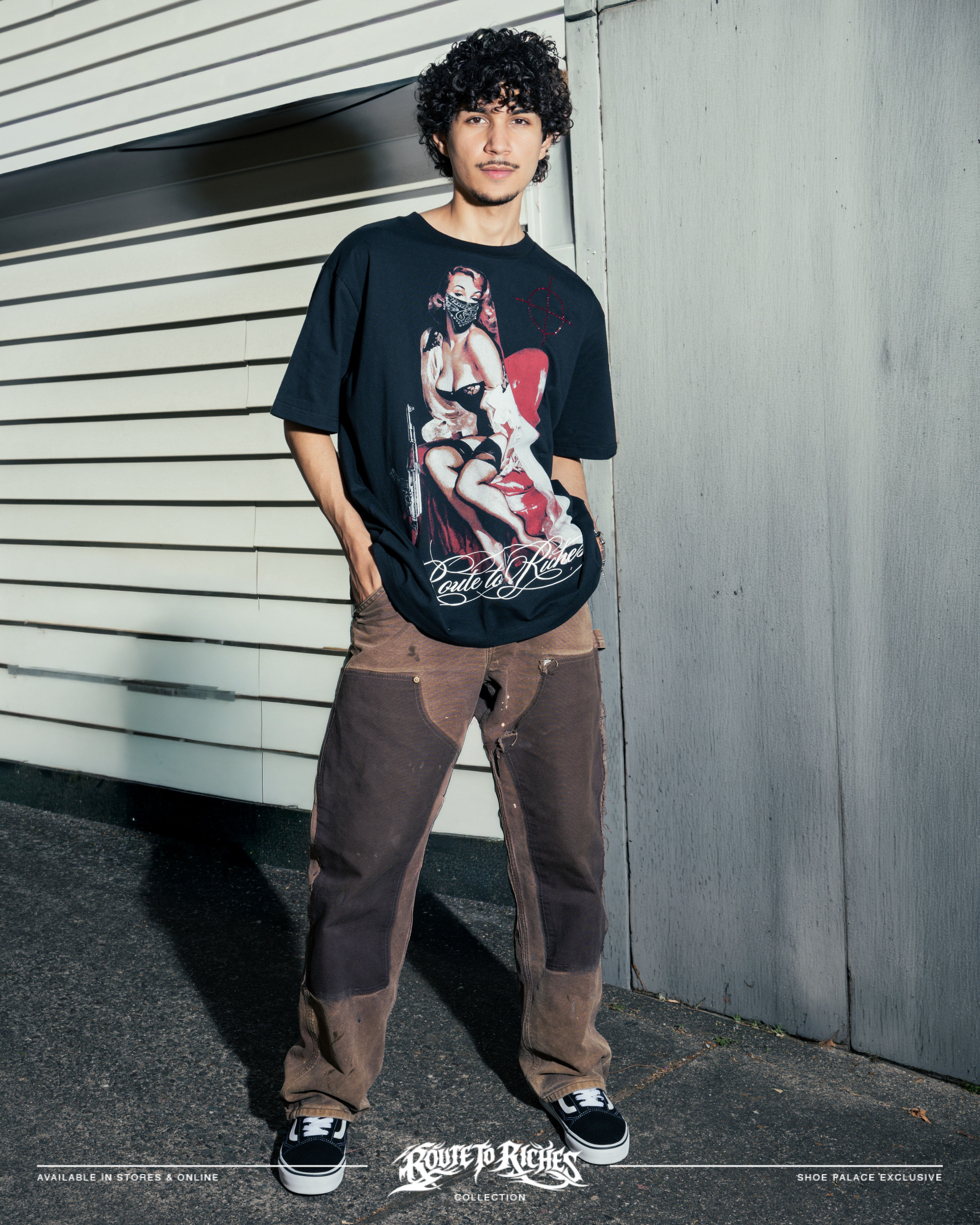 Person wearing graphic t-shirt and baggy pants, standing against a wall.