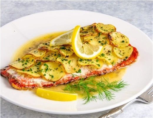 Baked fish with lemon and potato slices, garnished with herbs.