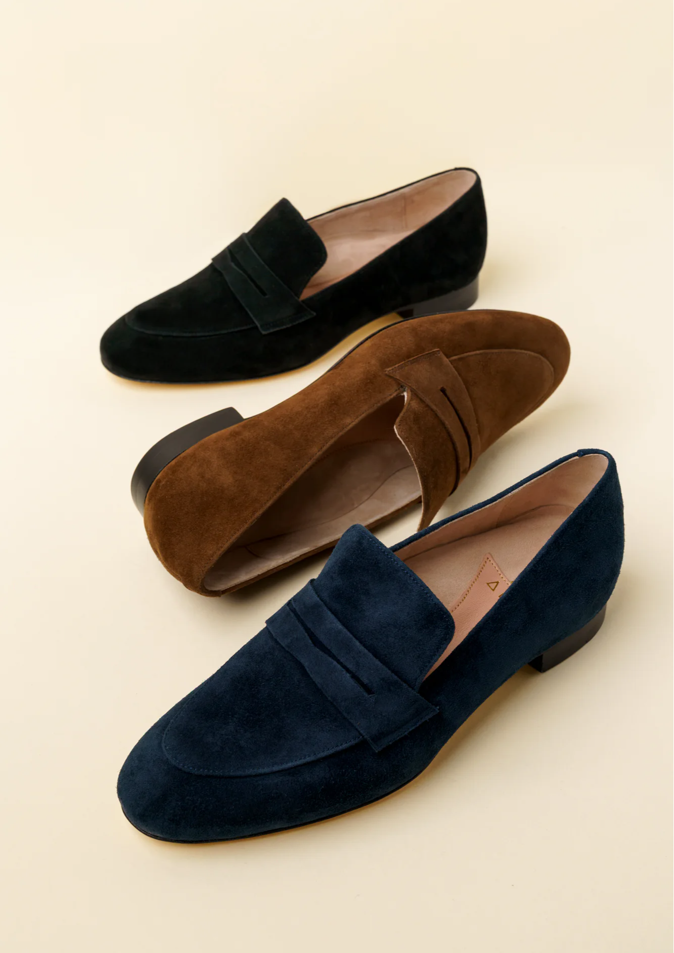 Three pairs of stylish suede loafers in black, brown, and navy.