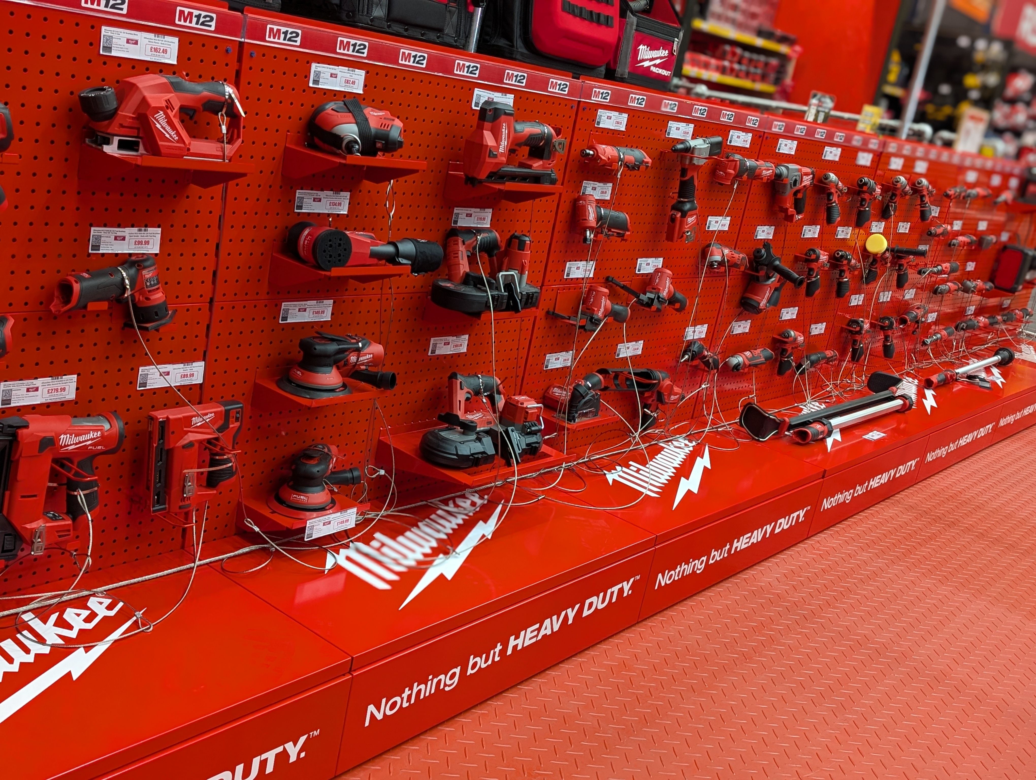 Display of various Milwaukee power tools on red background.