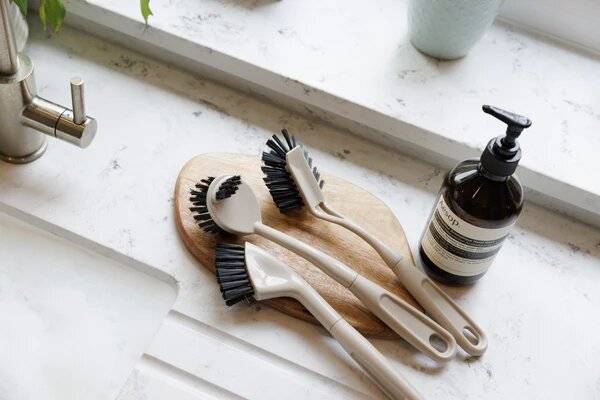 Three cleaning brushes on a wooden board next to a bottle of hand soap.