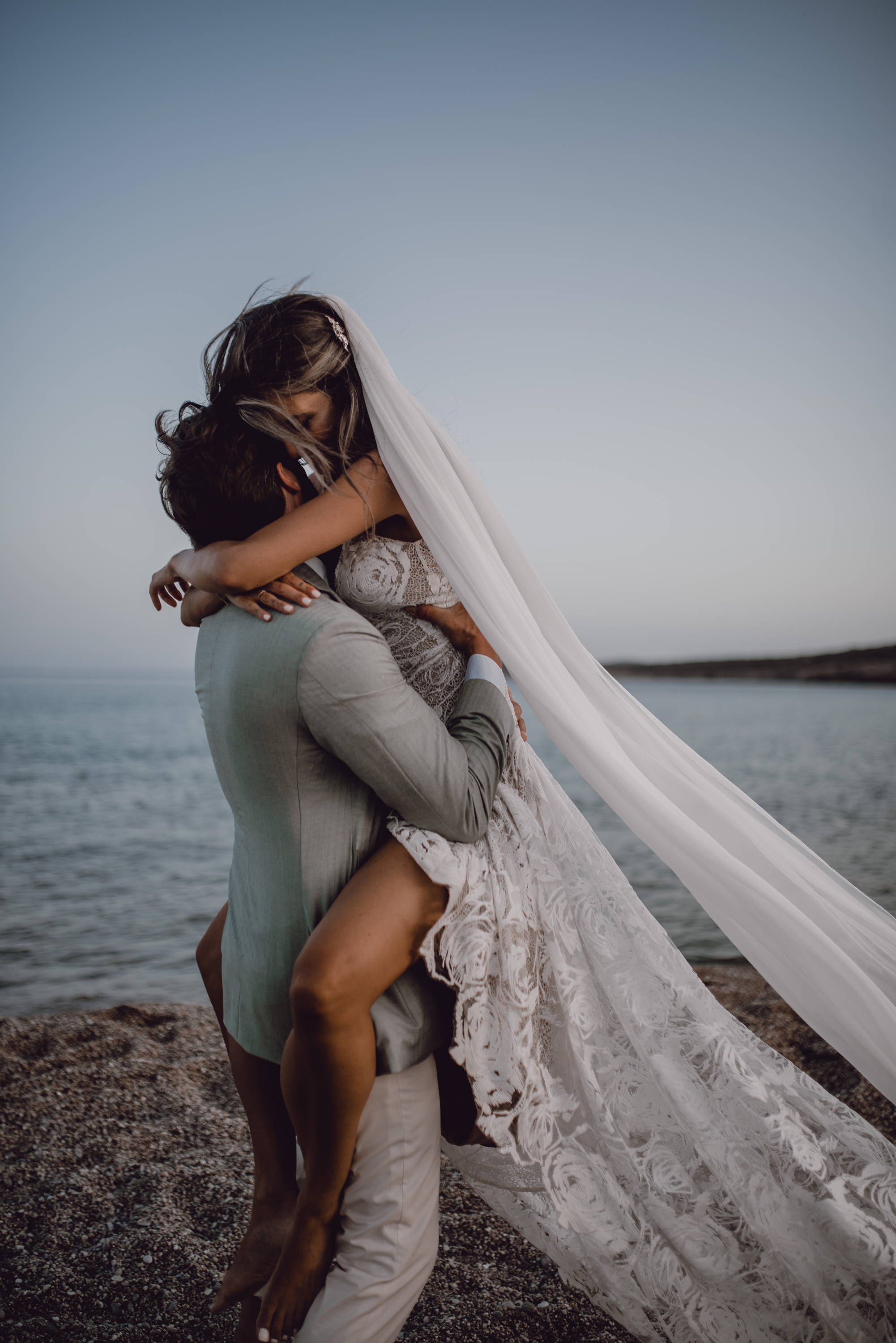 Groom hugging bride wearing a lace dress and veil