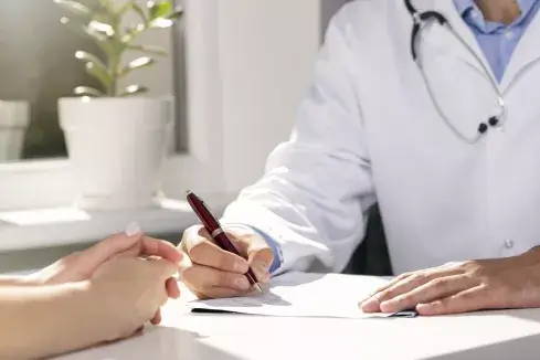 Een dokter aan tafel met een patiënt en schrijft wat op papier