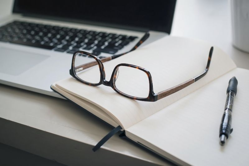 Trust Brown prescription glasses resting on an open notebook and pen placed on a desk