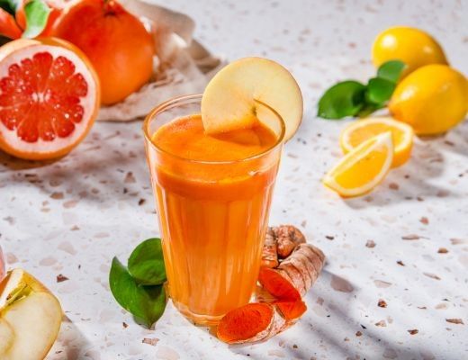 A glass of orange juice with fruit slices and green leaves.