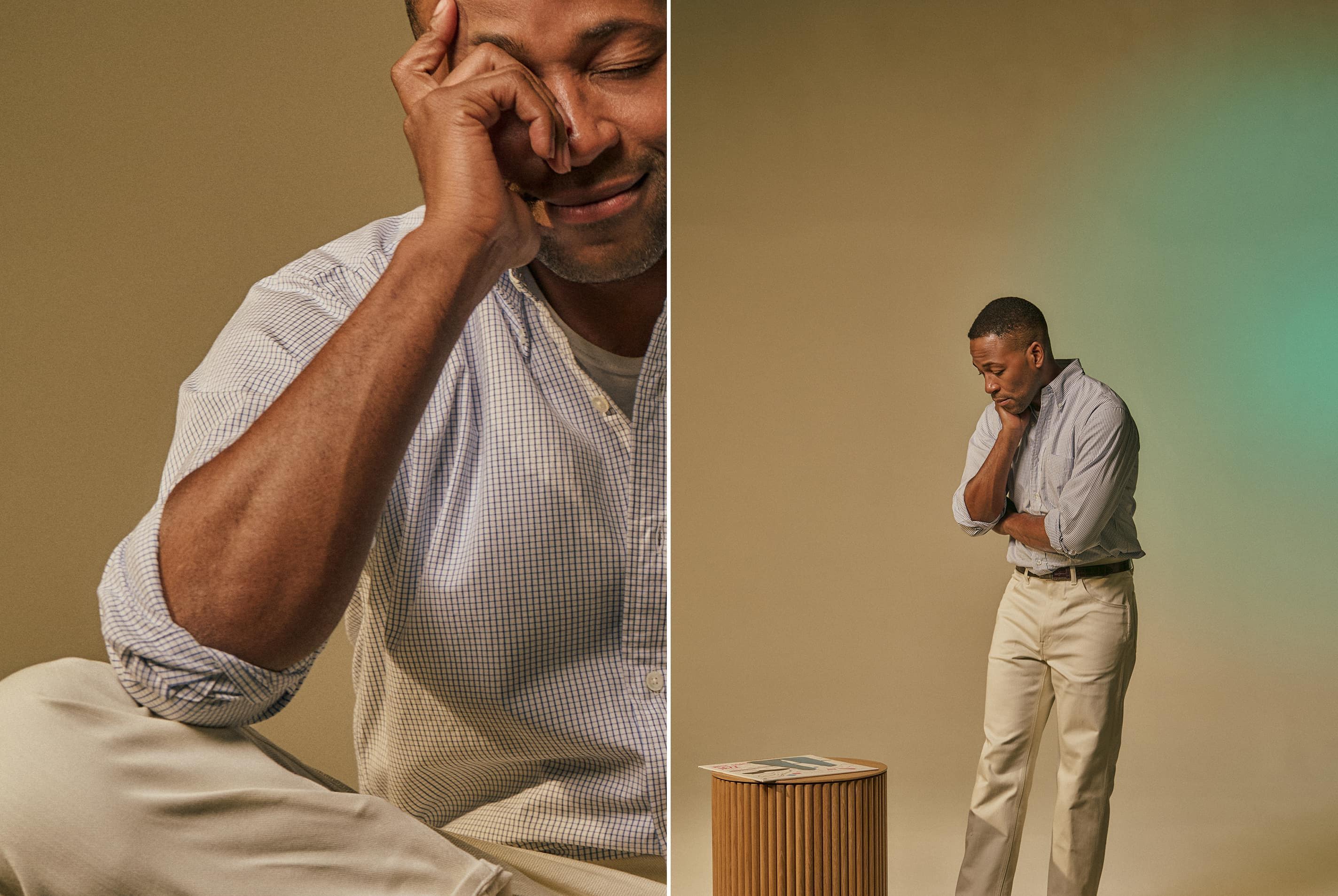 Man in casual attire appears thoughtful, standing beside a wooden stool.