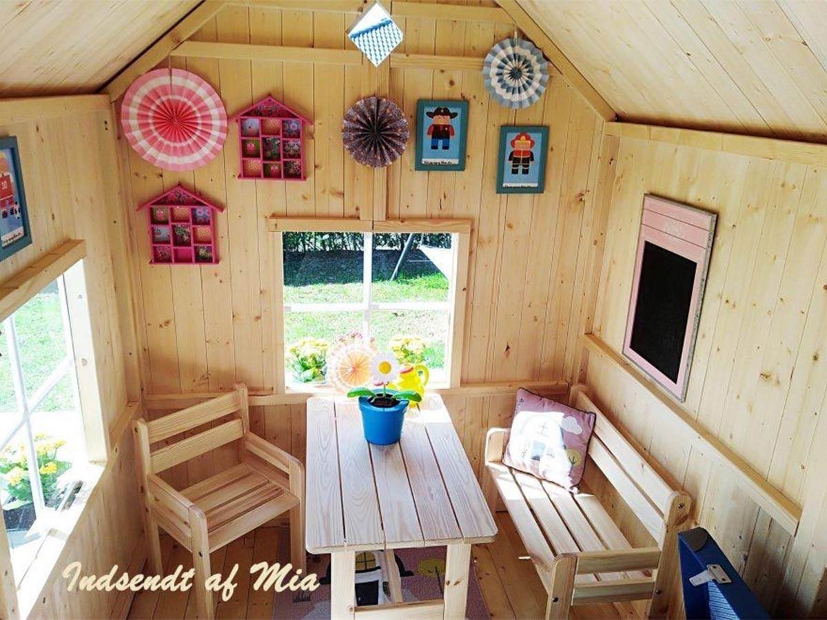 Inside of a wooden playhouse with kids furniture set and pictures and decorations on the wall by WholeWoodPlayhouses 