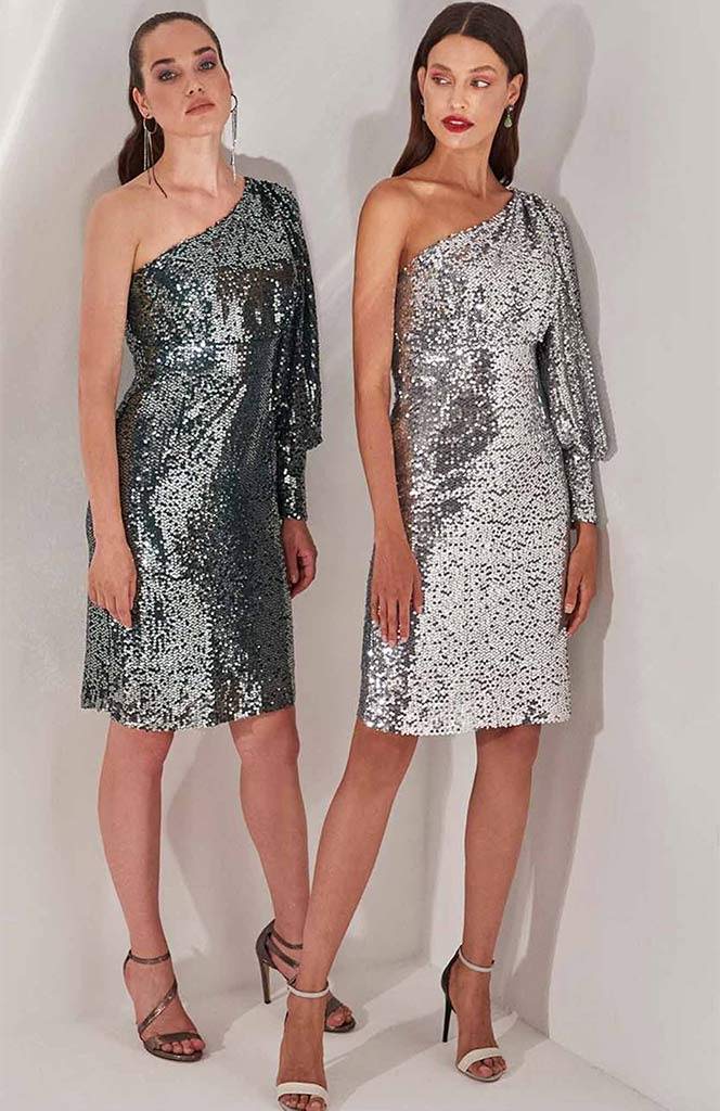 Two women in sequined one-shoulder dresses, silver and black, pose in a studio.