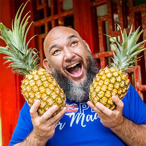 Smiling person holding two pineapples in front of a colorful background.