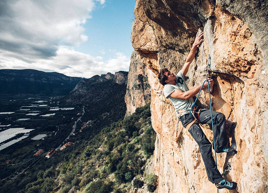 Ben rock climbing with a beautiful mountainscape in the background and blue sky with clouds