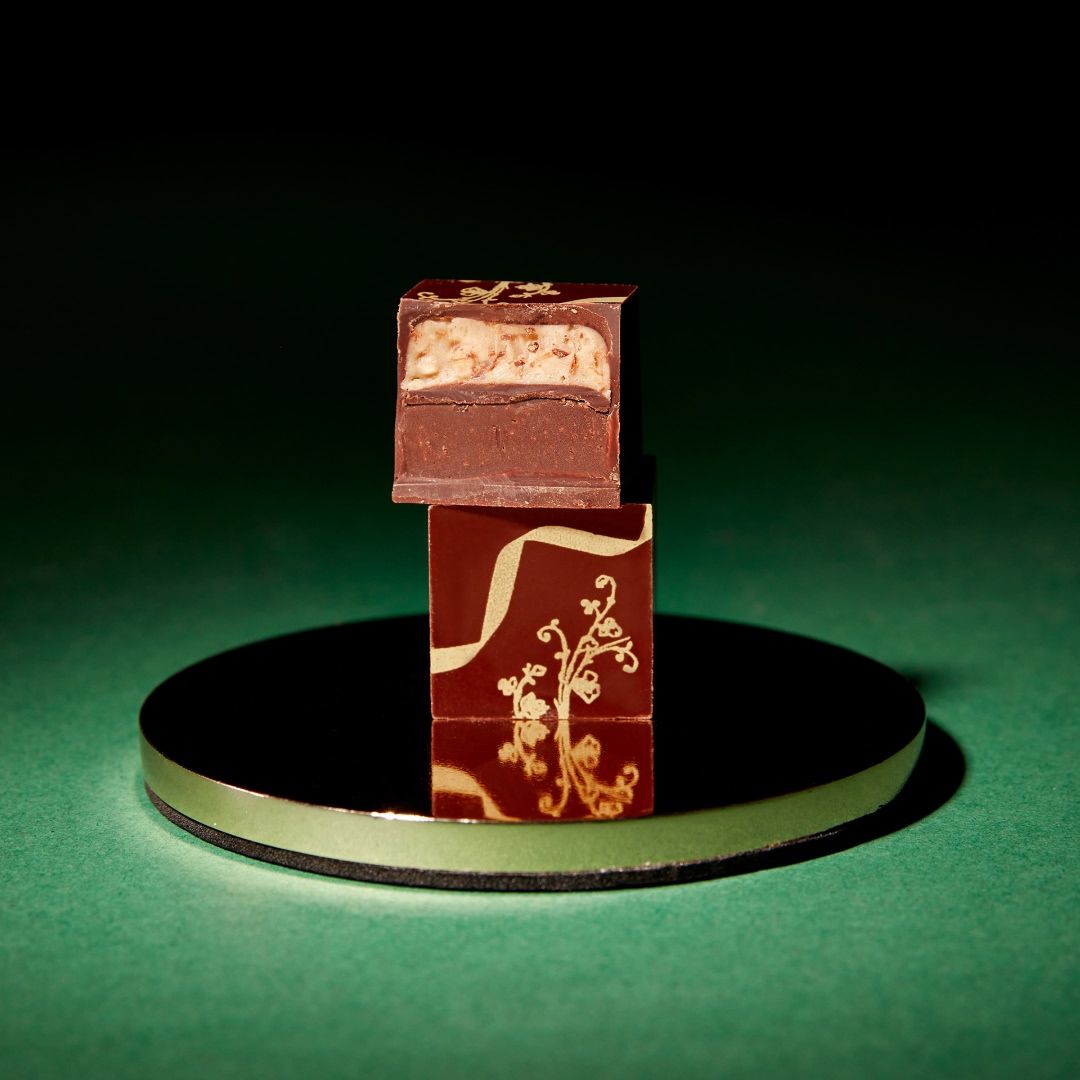 A piece of chocolate on a mirrored surface against a dark background.