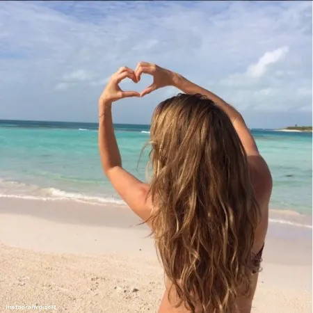 Girl on the beach with long wavy hair making a love heart with her hands