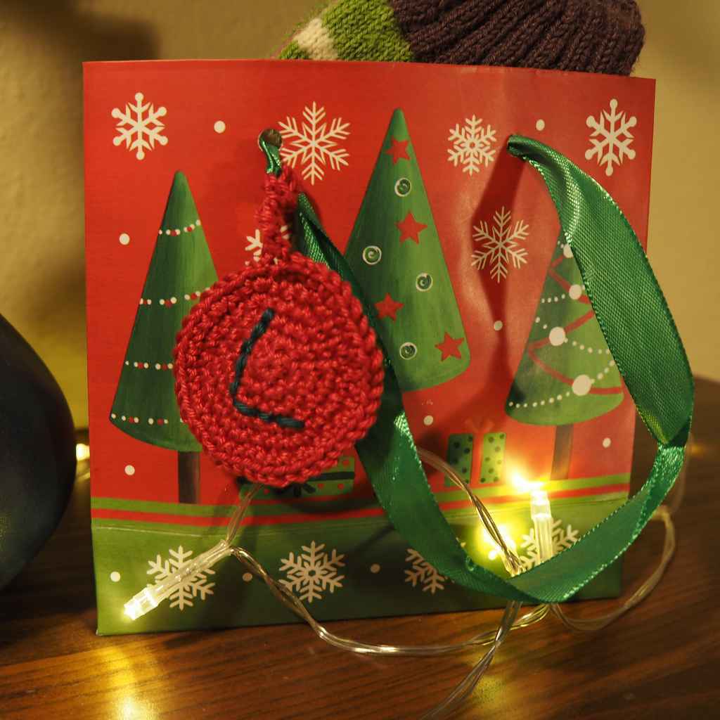 Gehäkelter roter Geschenkanhänger mit Initialen an einer Geschenkverpackung.