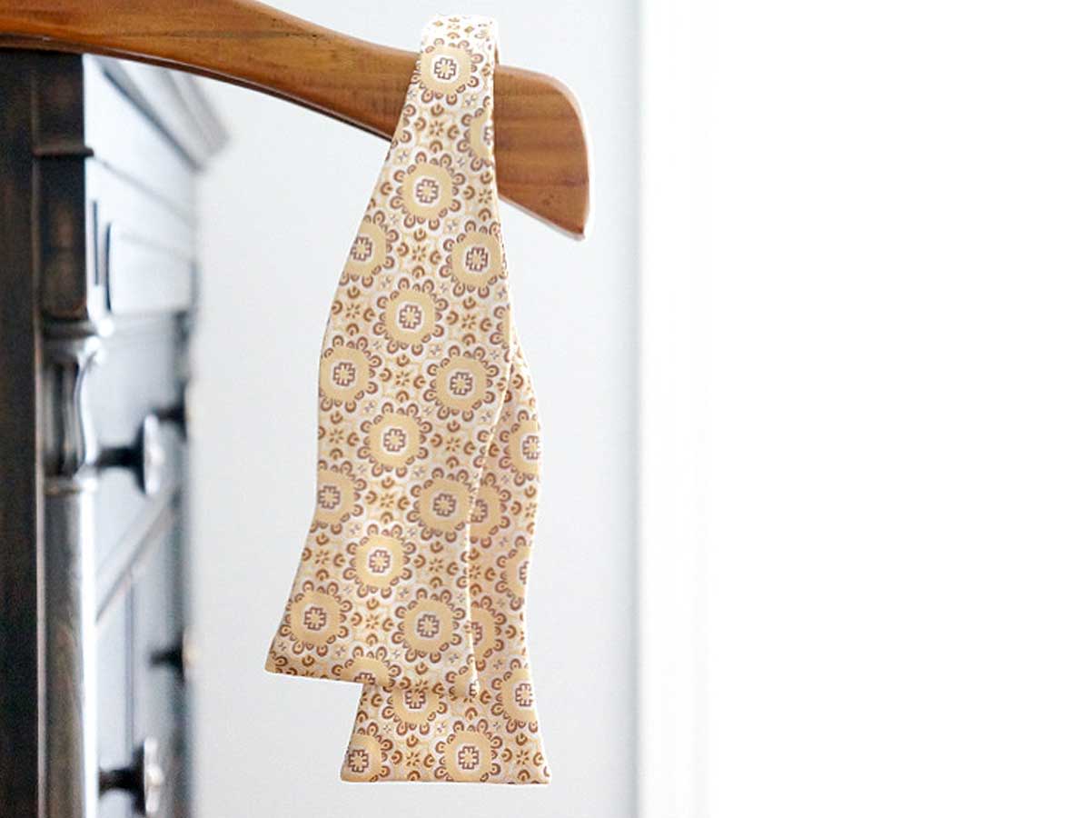 Abstract floral pattern self-tie bow tie, untied and hanging, in a yellow-beige color