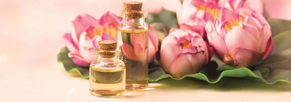 Bottles of oil beside pink lotus flowers on a green leaf.