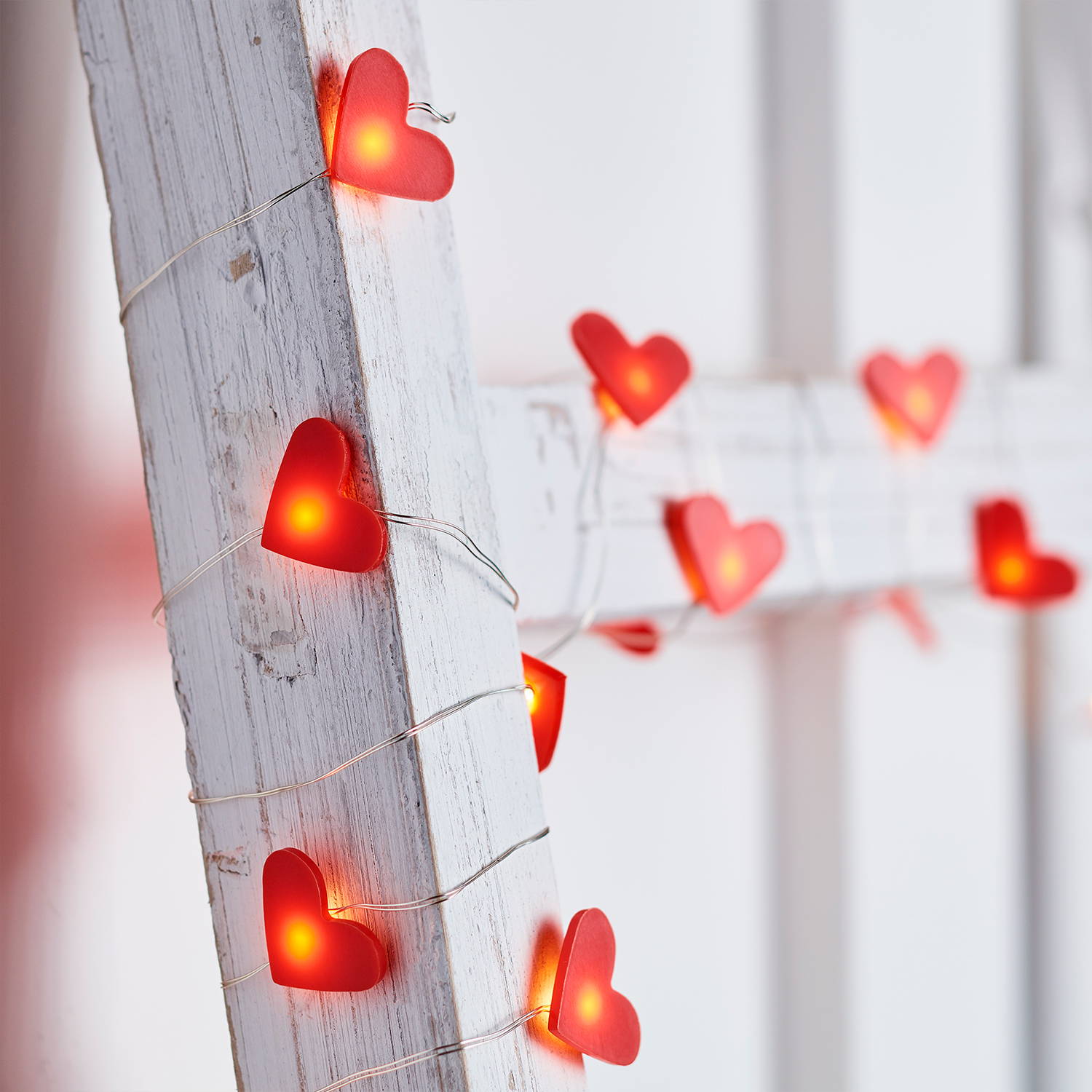 Red heart micro lights twisted around a white wooden ladder.