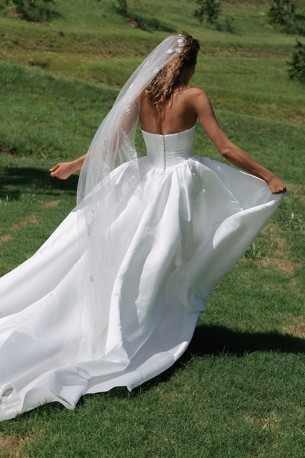 Bride in a flowing wedding dress with a veil, standing on green grass.