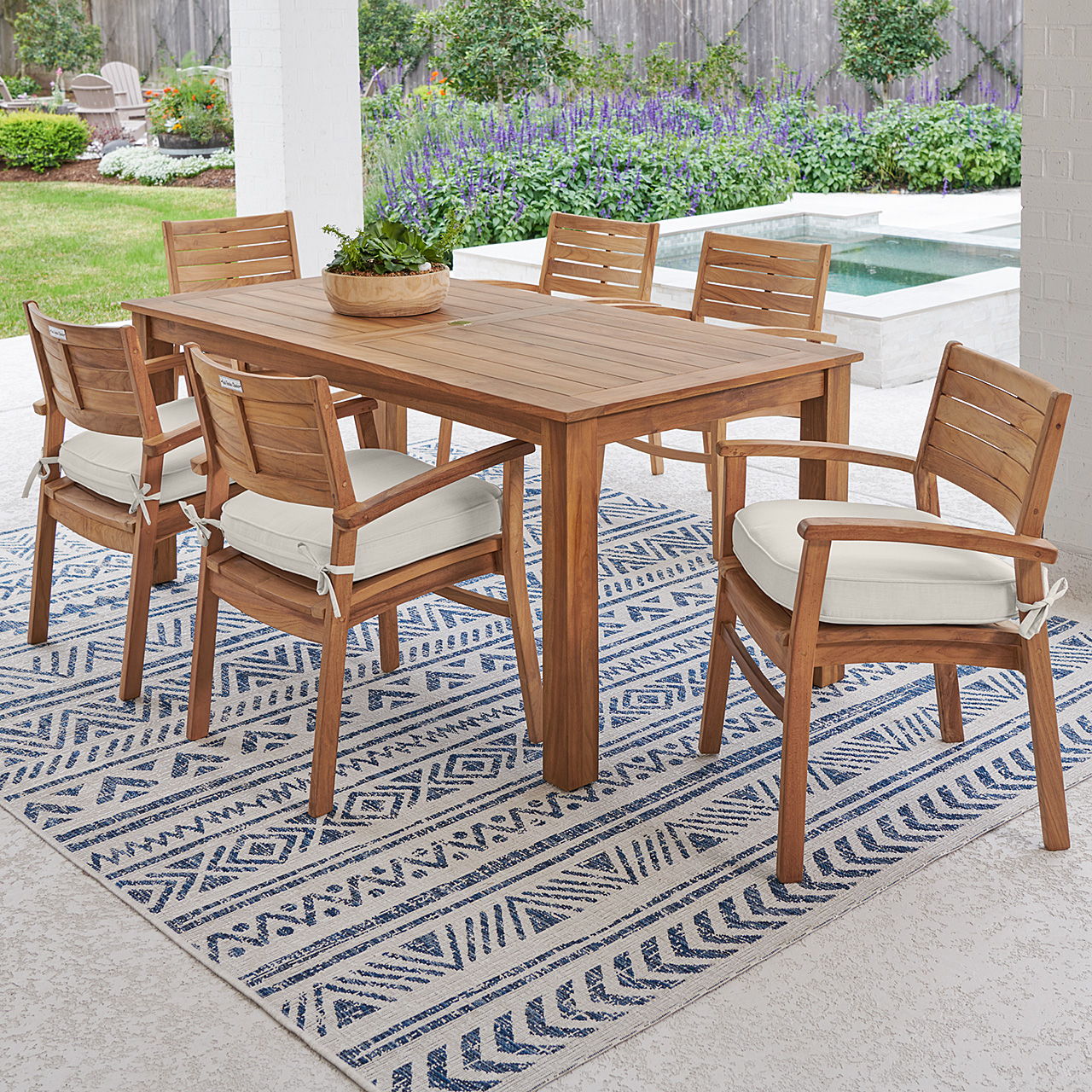 Outdoor dining table set with six chairs on a decorative rug.