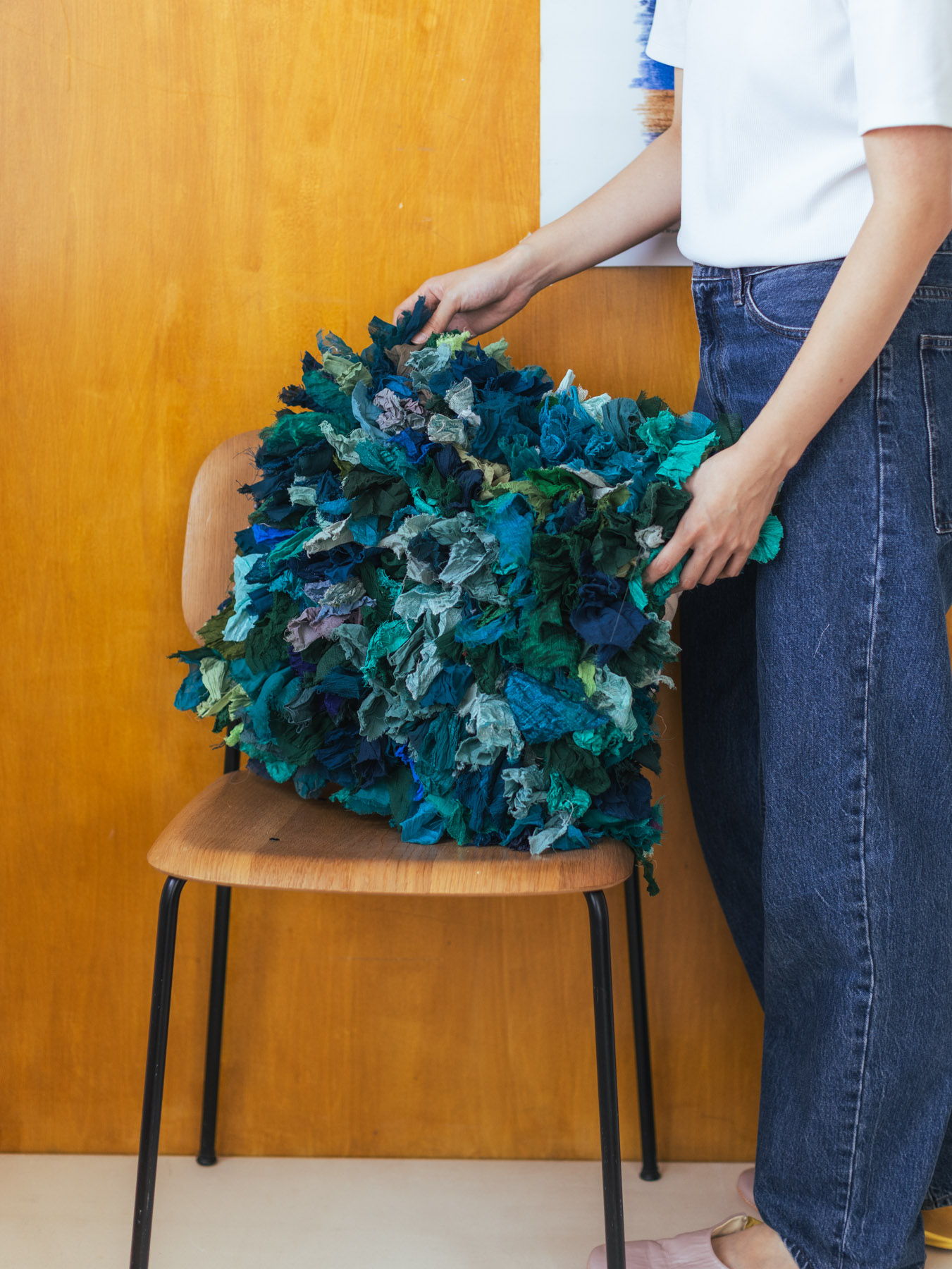 Person arranging a colorful, leafy cushion on a wooden chair.