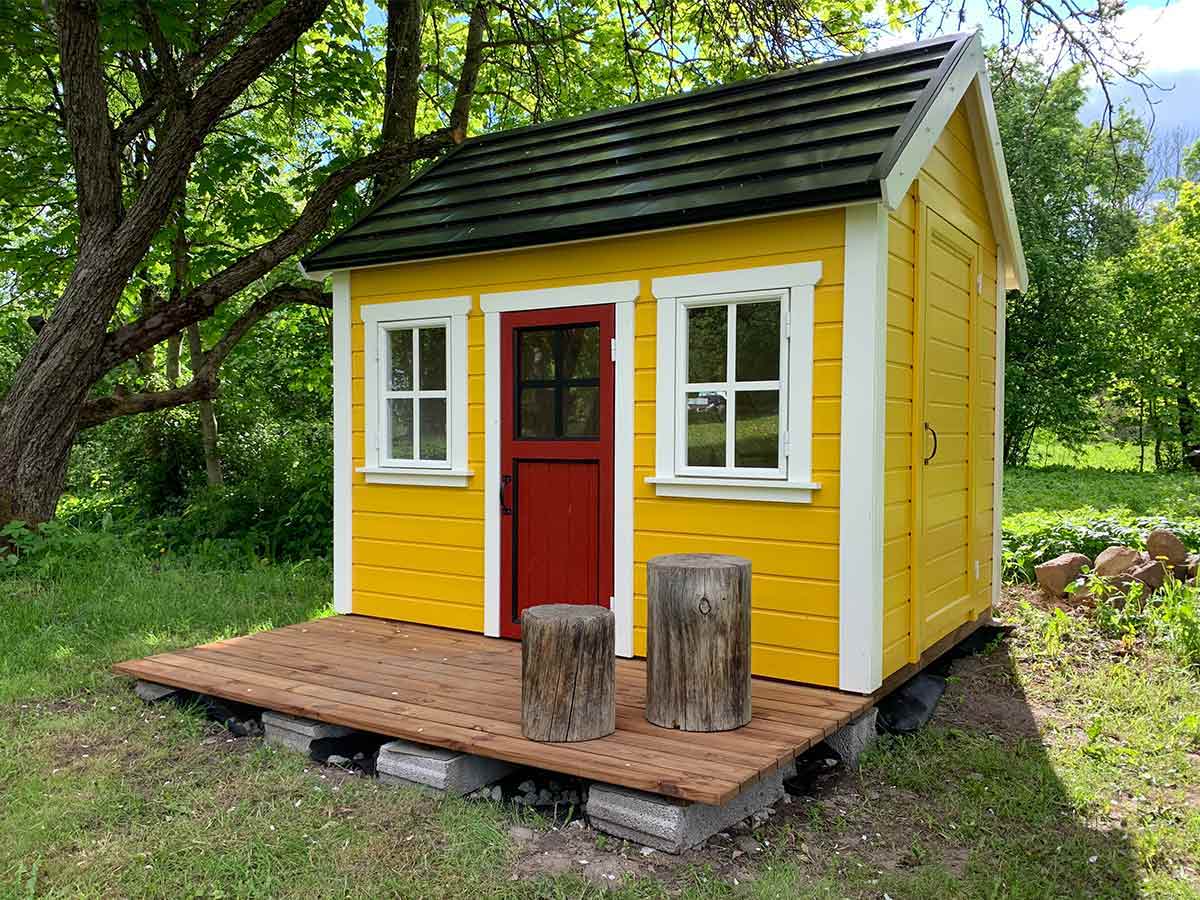 Yellow custom playhouse with a red wooden door in a green garden by WholeWoodPlayhouses
