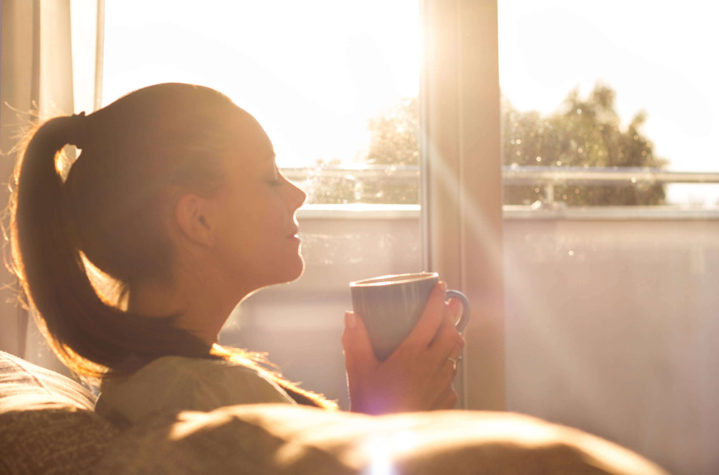 Woman enjoying morning coffee, woman sitting on the couch in the morning sun