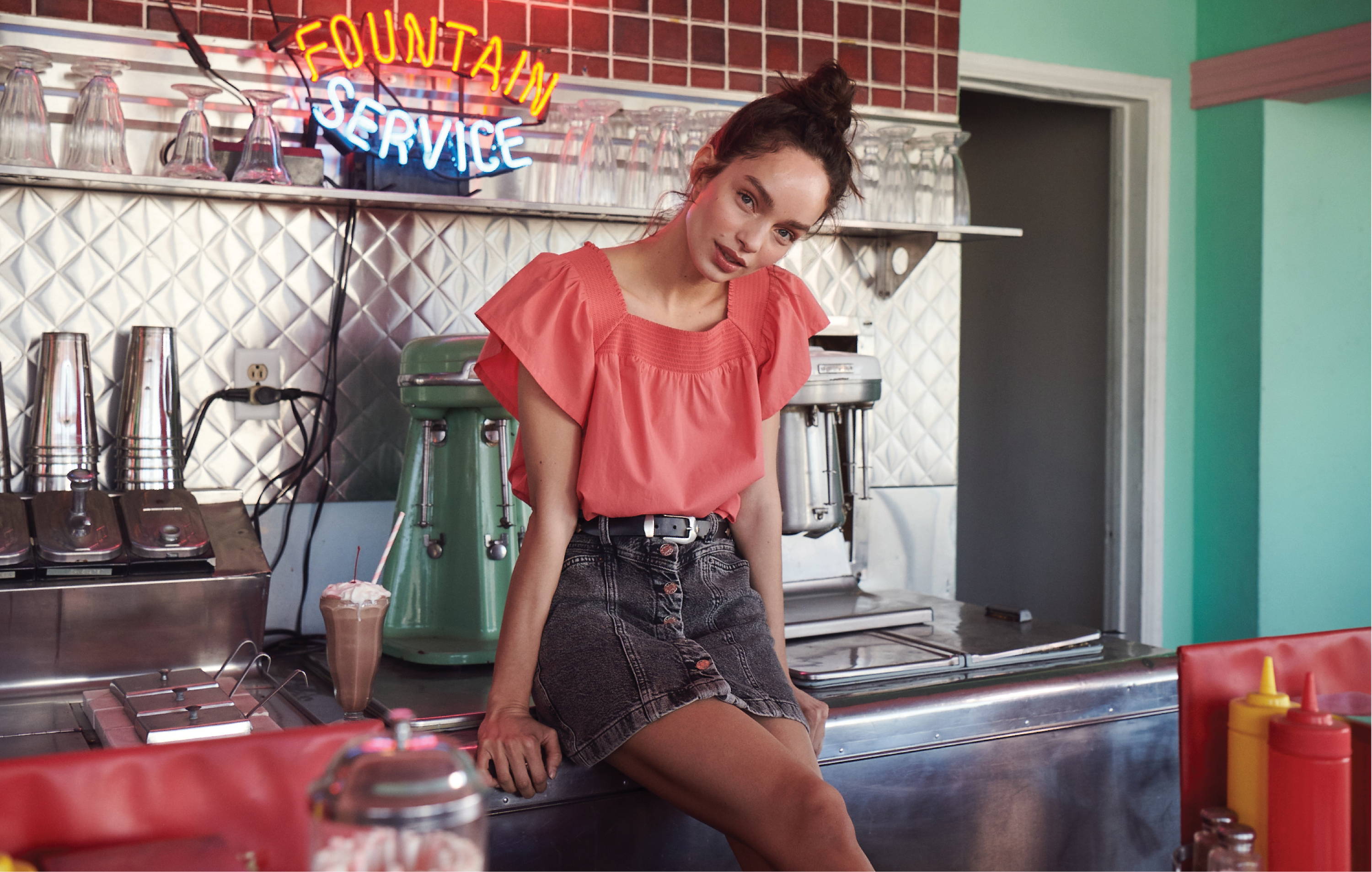 Model in diner where Sonora spiced coral shirt and Canyon skirt in acid black