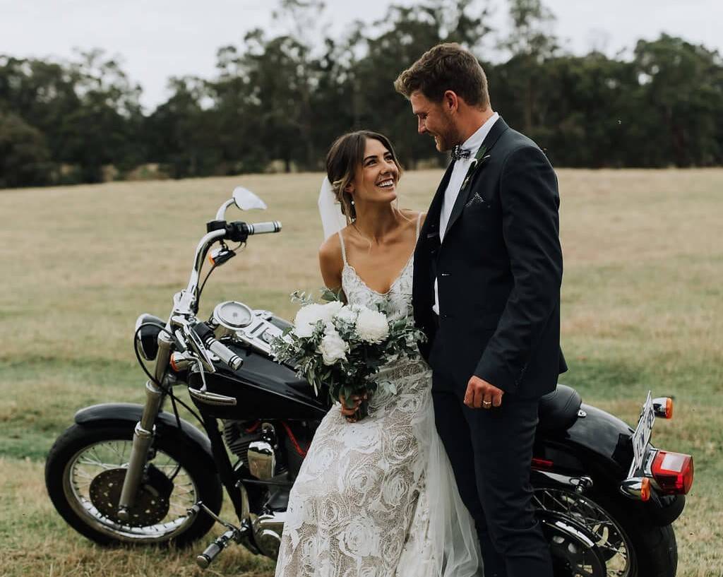 Bride wearing a rose lace dress and groom sitting on a motorcycle