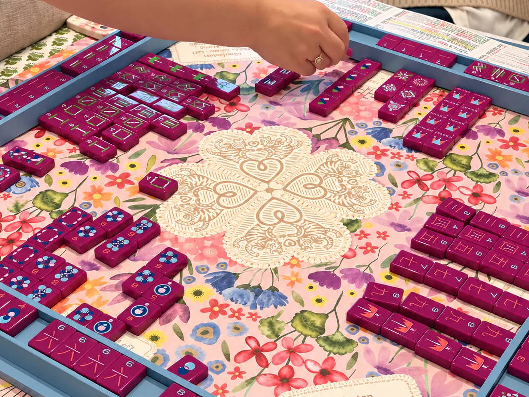 Colorful dominoes arranged on a floral tablecloth, with a player's hand reaching in.