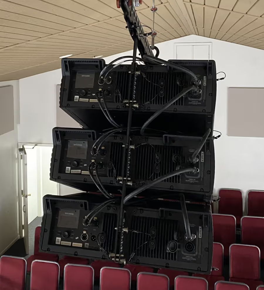 Stacked audio equipment suspended from the ceiling in an auditorium.