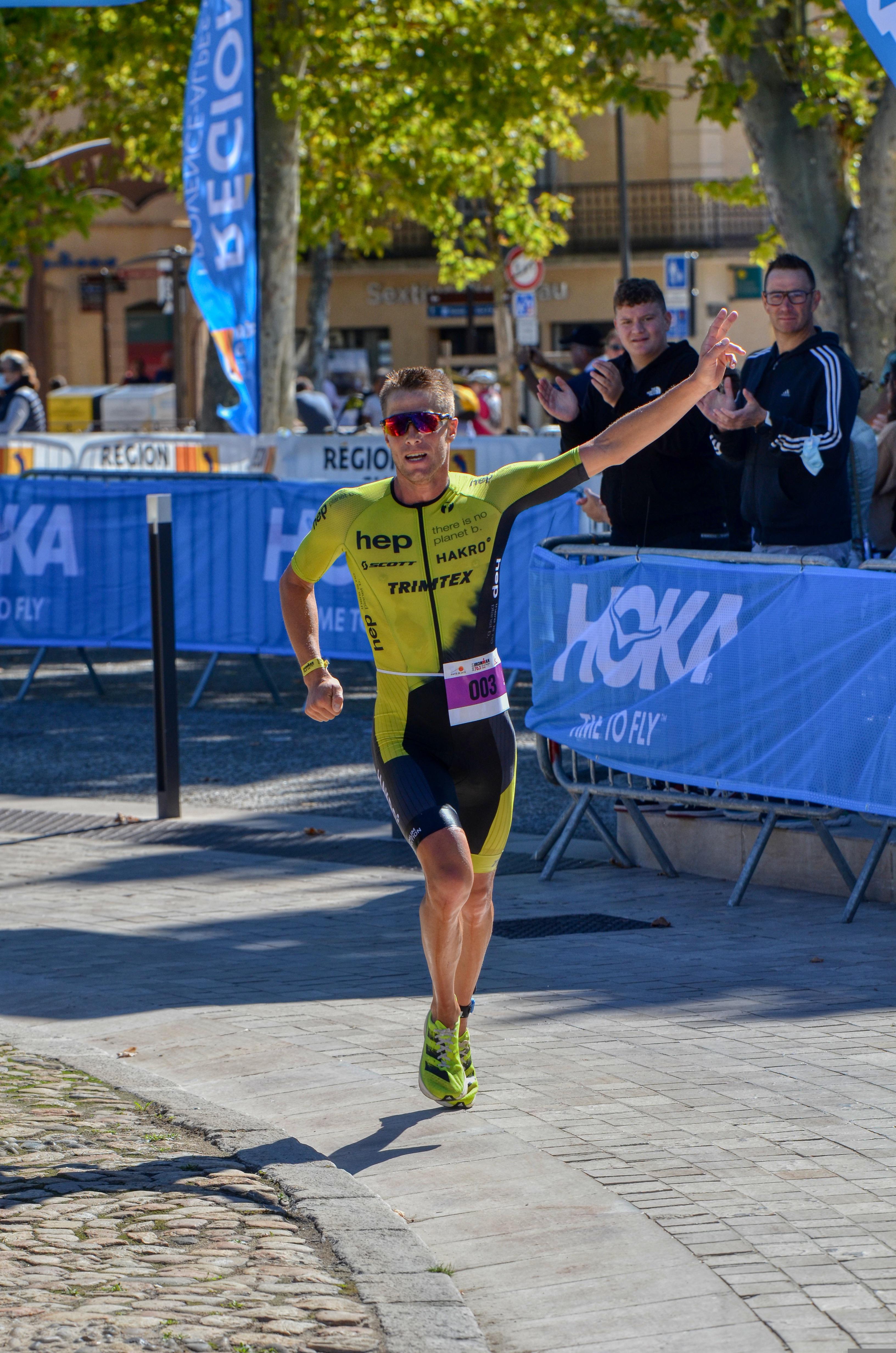 Ein Marathonläufer läuft frontal auf die Kamera zu und winkt dabei.