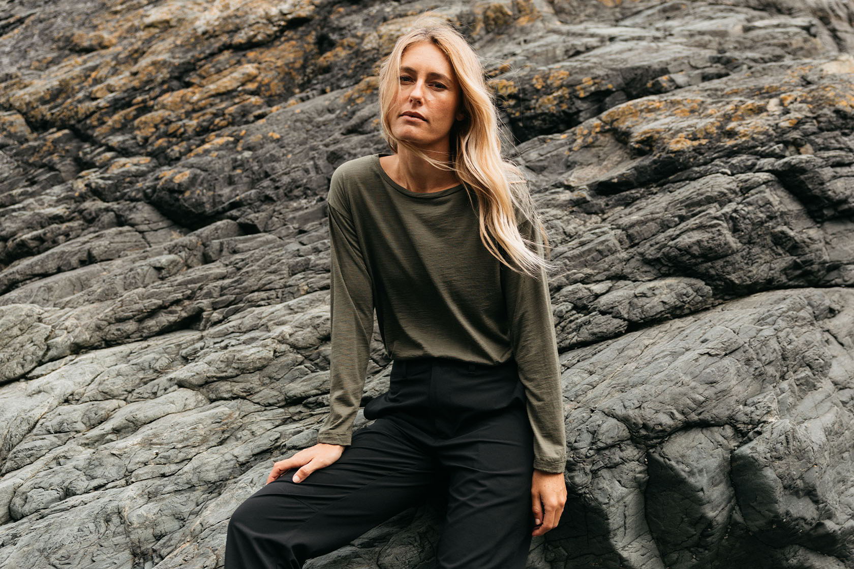Person sitting on rocks, wearing a long-sleeve top and black pants.