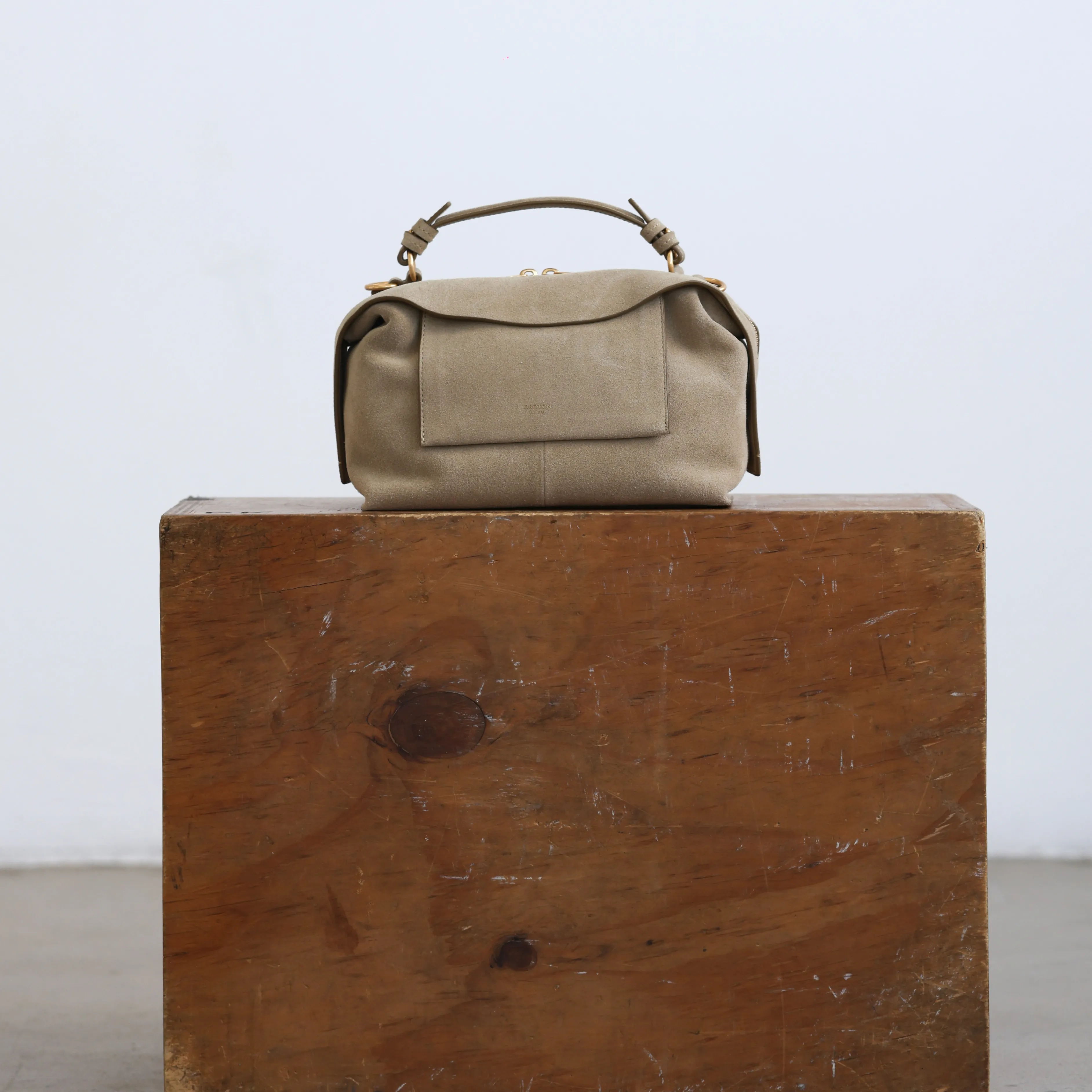 A beige bag resting on a wooden block against a plain background.