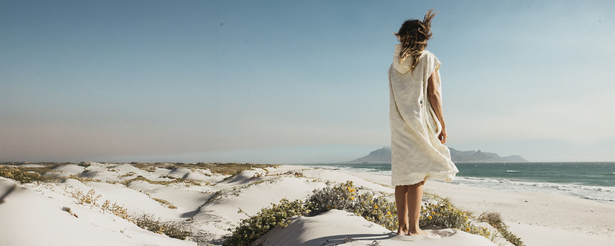 A woman in a white dress stands on a sandy beach.