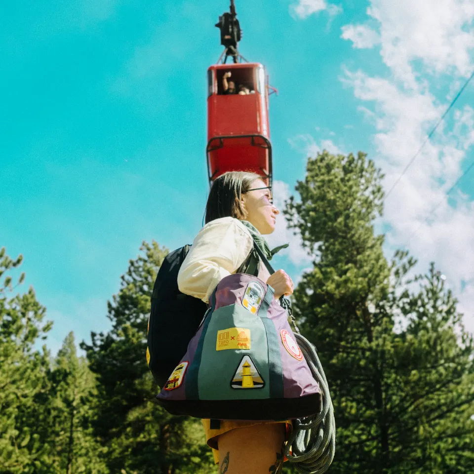 Person carrying a bag, looking up at a suspended object in nature.