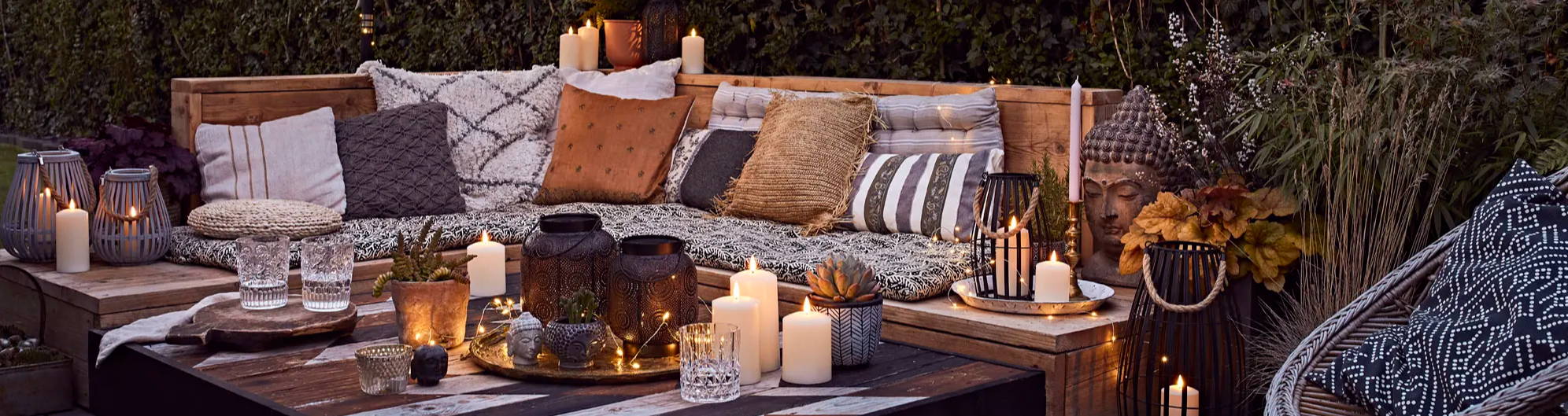 Terrassen Deko mit Outdoor LED Kerzen und Kissen auf Sitzbank.