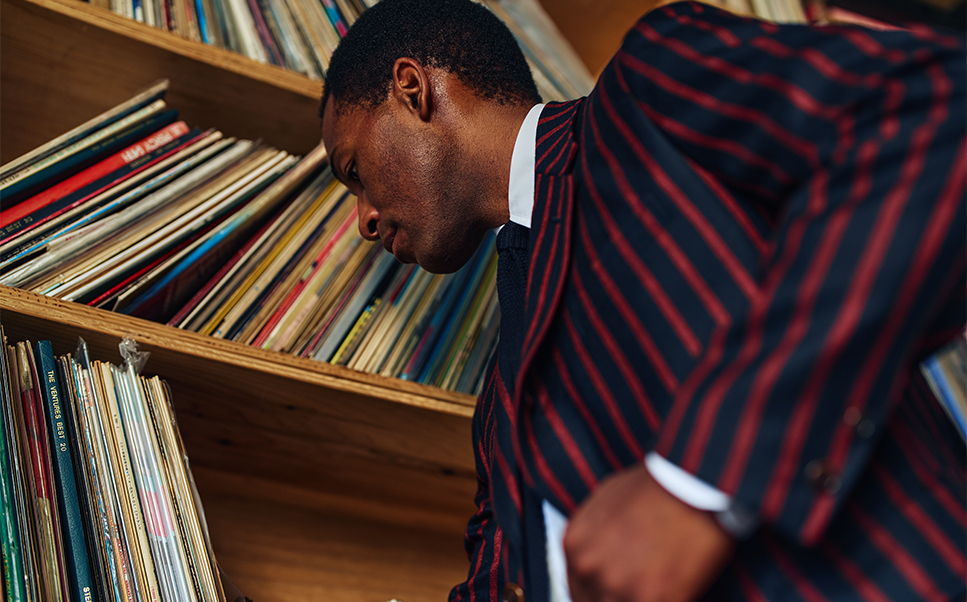 A man in a striped suit looks at records on a shelf.